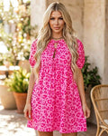 Woman wearing a pink leopard print dress with puff sleeves and tie front.